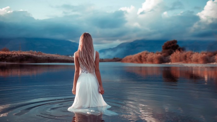 Woman in white dress standing in a lake at sunset