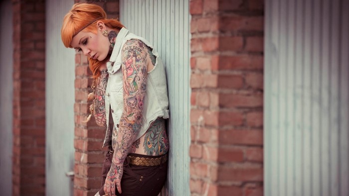 Woman with extensive tattoos leaning against a wall