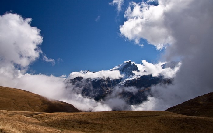 Mountain peaks emerge from clouds over a grassy hillside