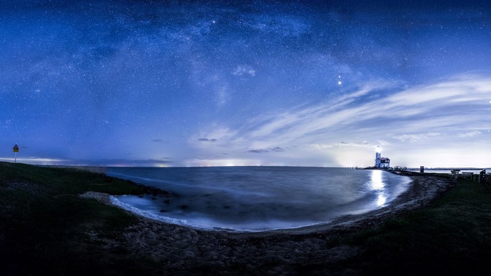 Night sky over the sea with a lighthouse
