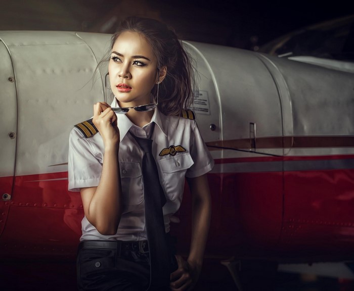 Asian woman pilot posing by airplane