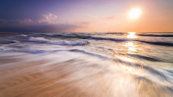 Long exposure of waves crashing on a sandy shore at sunset