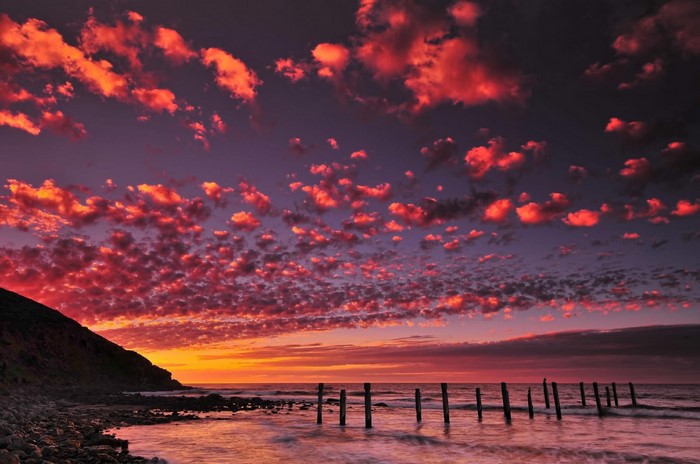 Sunset over the sea with red clouds and wooden posts