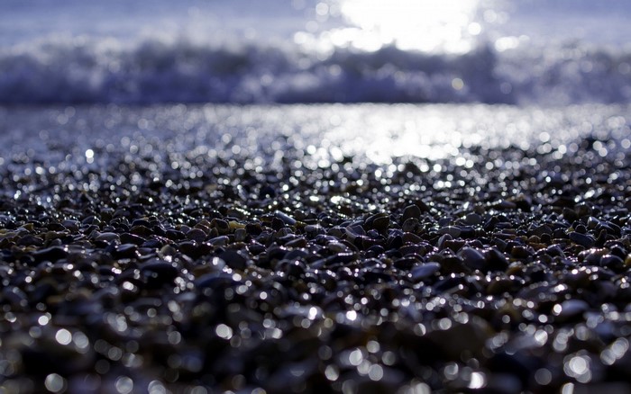 Pebble beach with sunlight reflecting on wet stones and waves