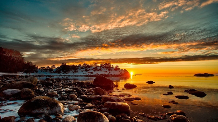 Sunset over a rocky shore with snow-covered trees