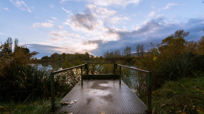Metal platform on a lake with autumn foliage and clouds