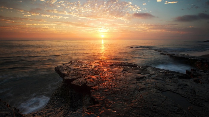 Sunset over the ocean with rocky shore