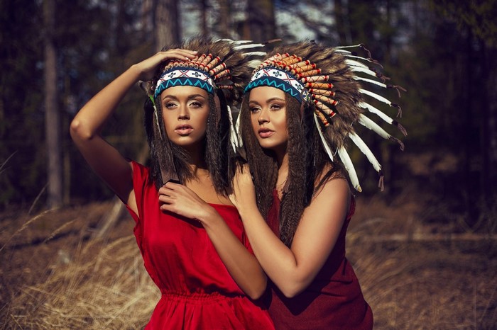 Two women wearing Native American headdresses in a forest