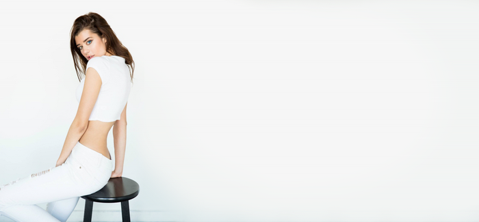 Sarah McDaniel in white crop top and jeans sitting on stool