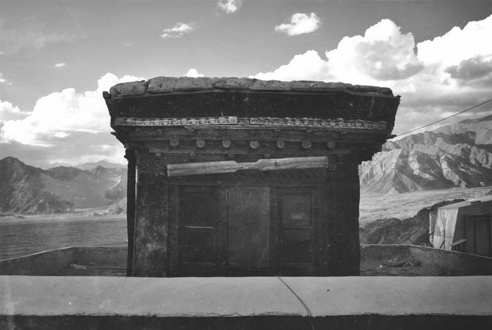 Monochrome photograph of a Tibetan temple structure with mountains in the background
