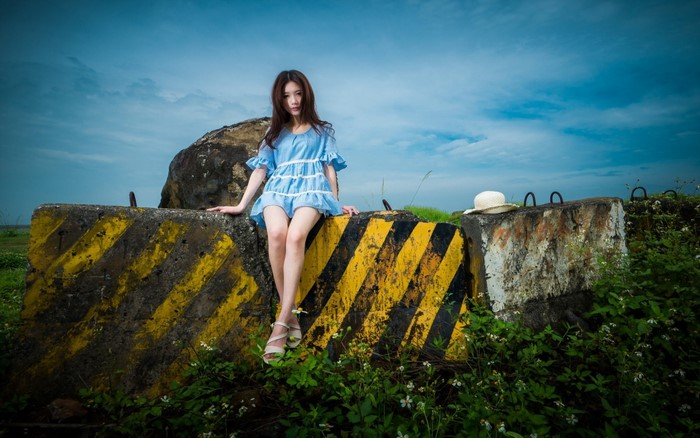 Young Asian woman in blue dress sitting on concrete barrier