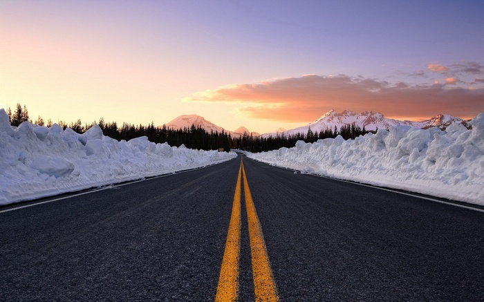 Road through snow-covered mountains at sunset