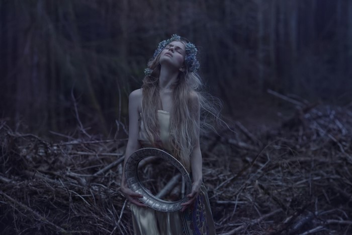 Woman with flower crown holding a mirror in a forest