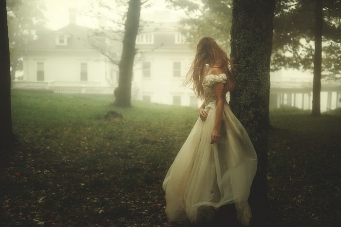 Woman in a dress by a tree with a house in the fog