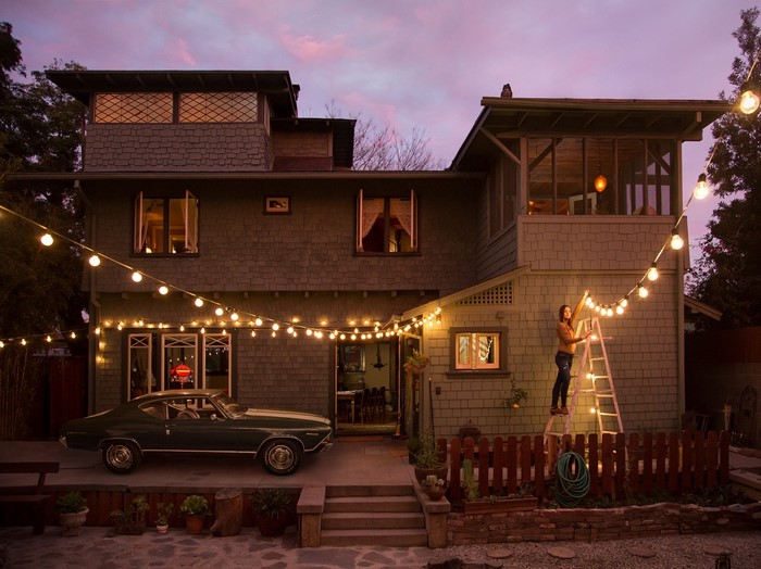 Woman hangs string lights on a house with a vintage car