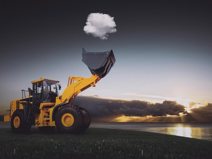 Yellow front loader lifting a cloud over the sea at sunset
