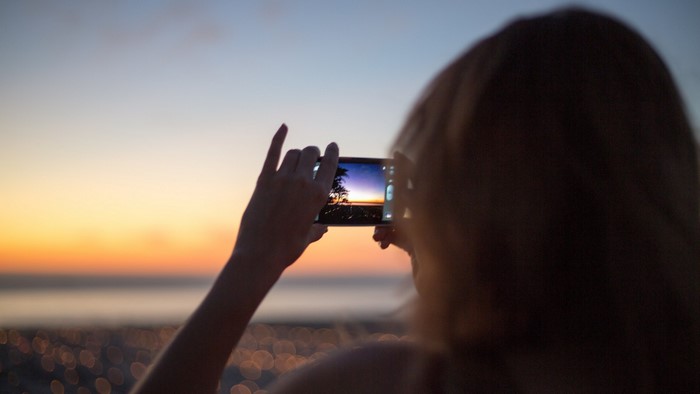 Woman taking a photo of a sunset with her phone
