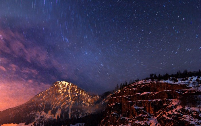 Star trails over snow-covered mountains at night