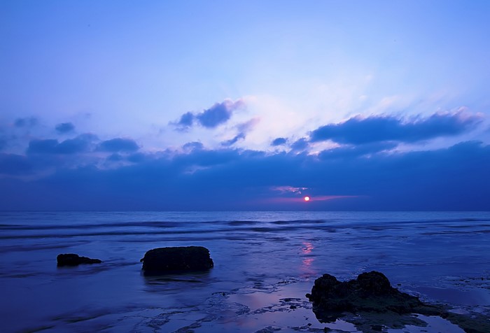 Sunset over the ocean with clouds and rocks on the shore