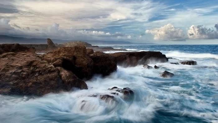 Waves crashing on rocky shore with cloudy sky