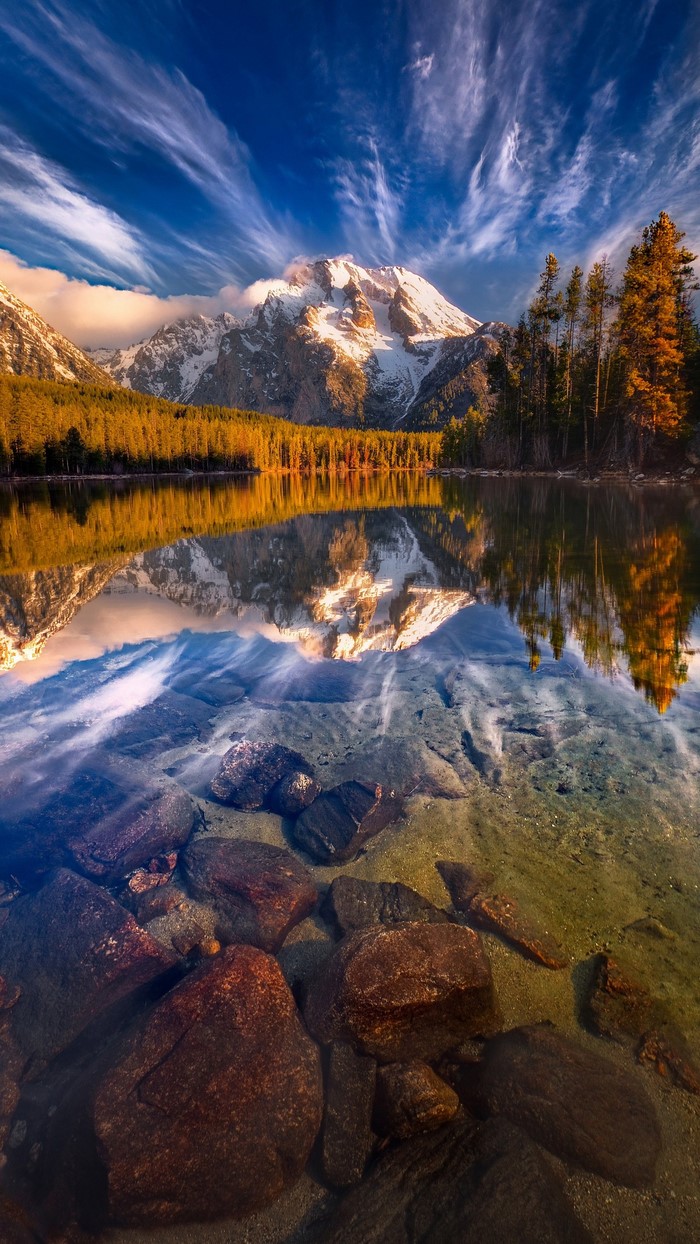 Mountain lake reflection at sunrise with snow-capped peaks and autumn trees