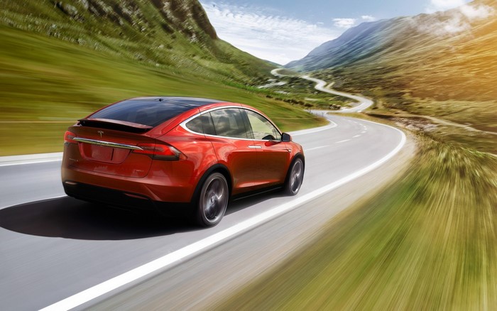 Red Tesla Model X driving on a winding mountain road