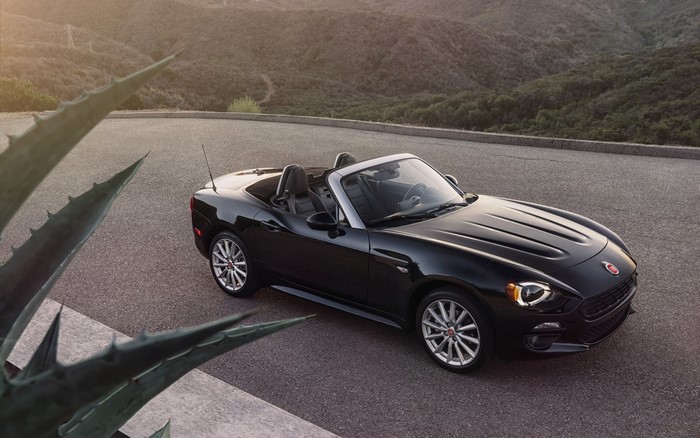 Black Fiat 124 Spider convertible parked on a mountain road