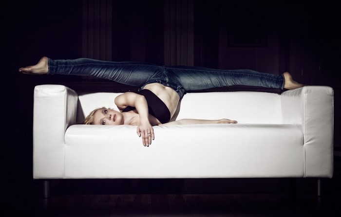 Woman in jeans doing a split on a white couch