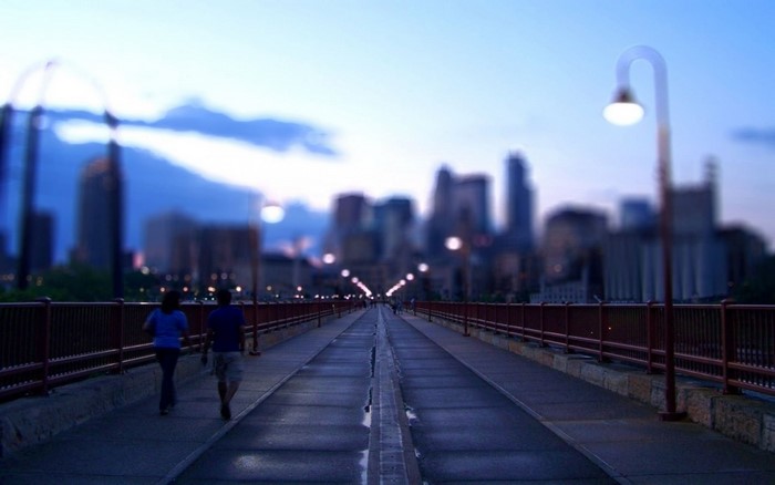 People walking on a bridge towards a city skyline at dusk
