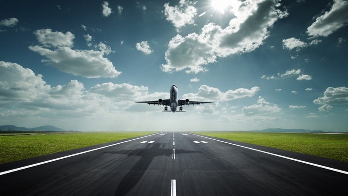 Airplane taking off from runway with clouds and sun