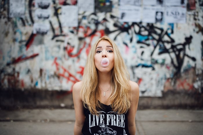 Woman blowing bubblegum in front of graffiti wall