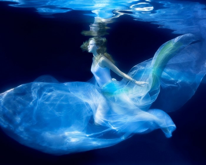 Woman in white dress underwater with flowing fabric