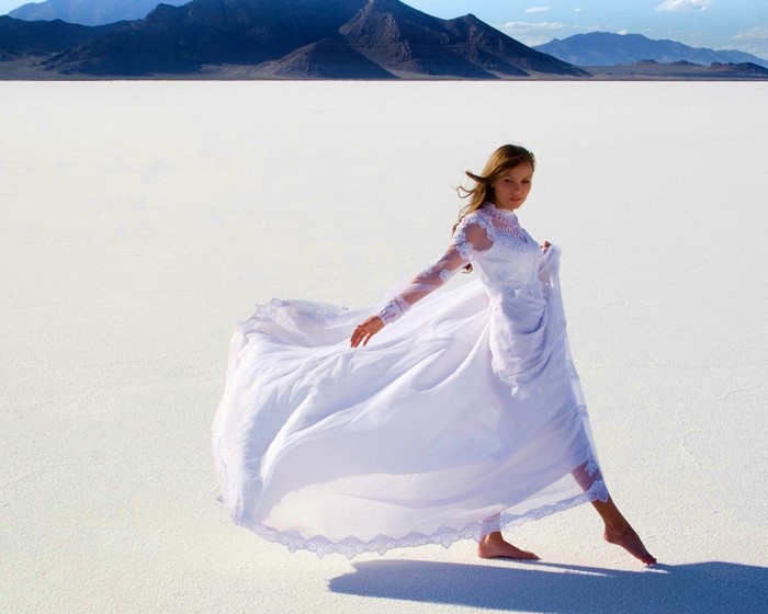 Woman in white dress on salt flats with mountains