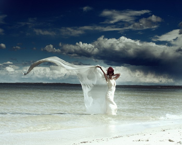 Woman in white dress holding white fabric on a beach