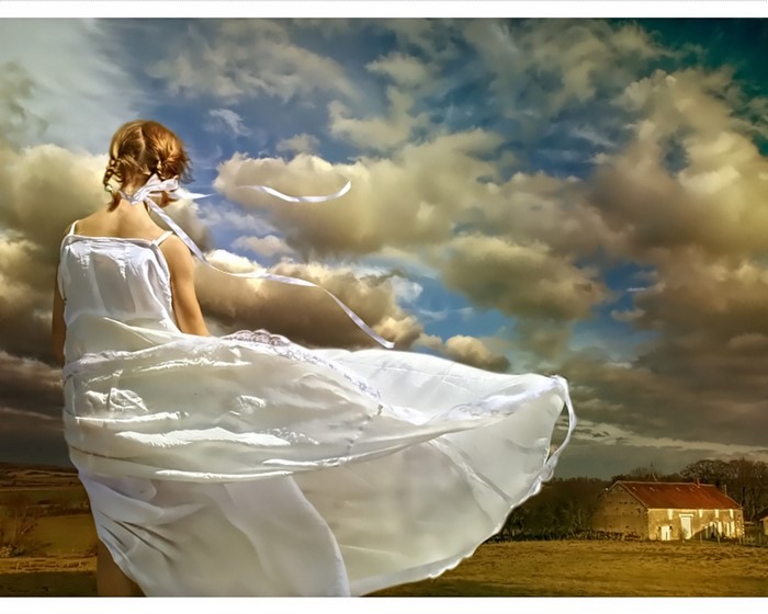 Woman in white dress in a field with dramatic clouds