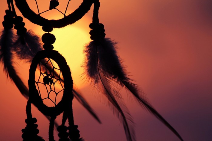 Silhouette of dreamcatchers with feathers against sunset