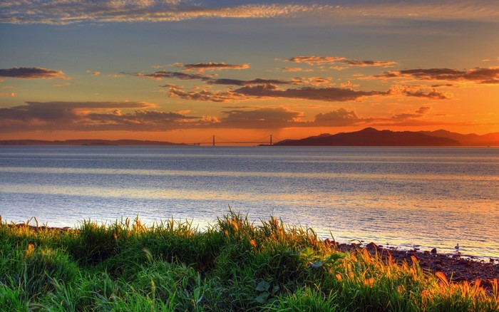 Sunset over the sea with a distant bridge and mountains