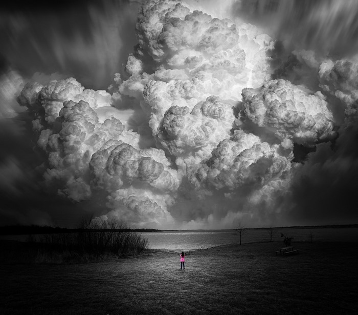Woman in pink stands before a massive cloud formation over water