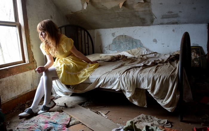Woman in yellow dress sitting on a bed in an abandoned room