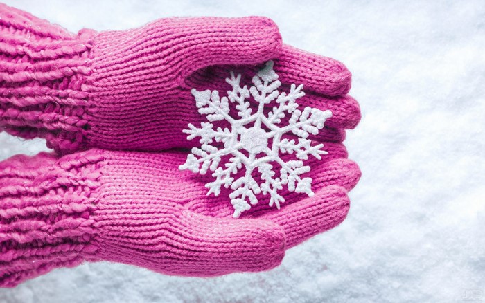 Pink knitted gloves holding a snowflake