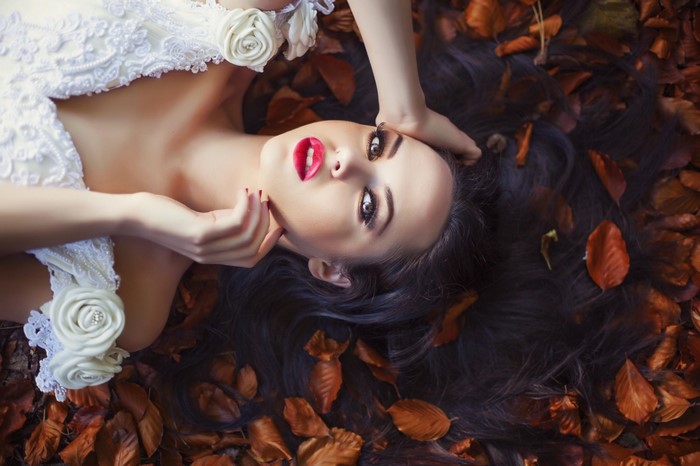 Woman in white dress lying on autumn leaves