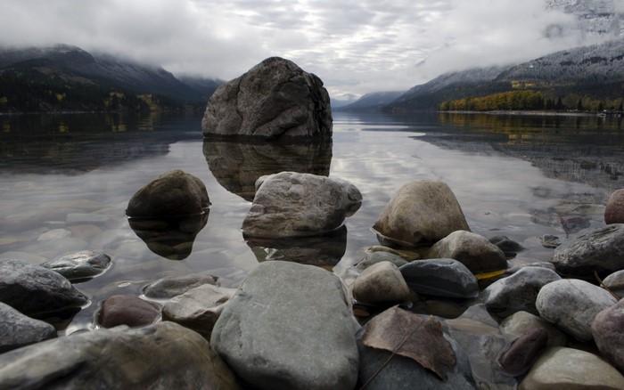 Rocks in a lake with mountains and cloudy sky