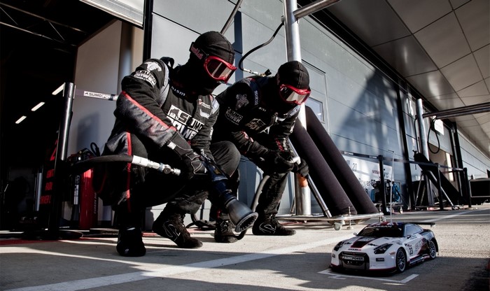 Two people in racing suits with a toy Nissan GT R NISMO