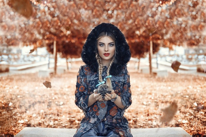 Woman in hooded coat holding a hedgehog in autumn park