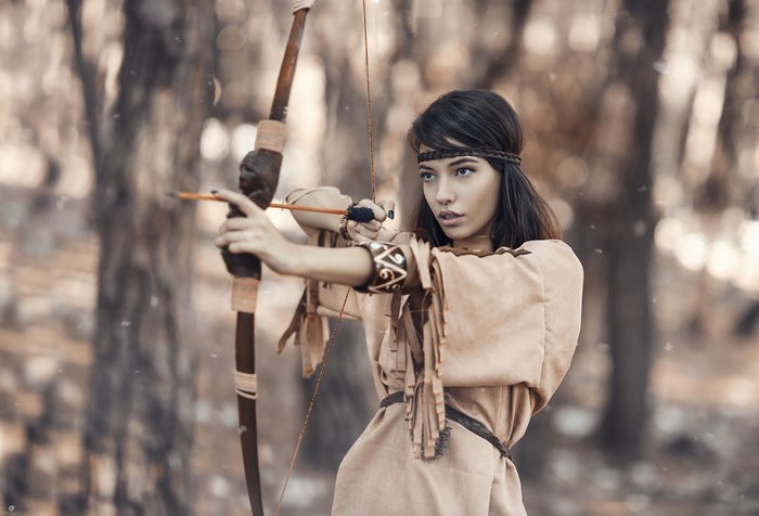Woman in Native American attire aiming a bow and arrow