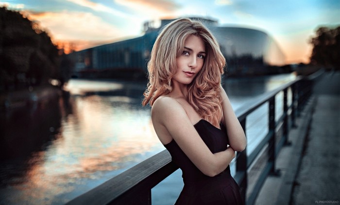 Woman in black dress posing on a bridge at sunset