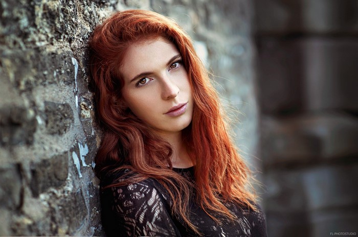 Woman with long red hair leaning against a stone wall