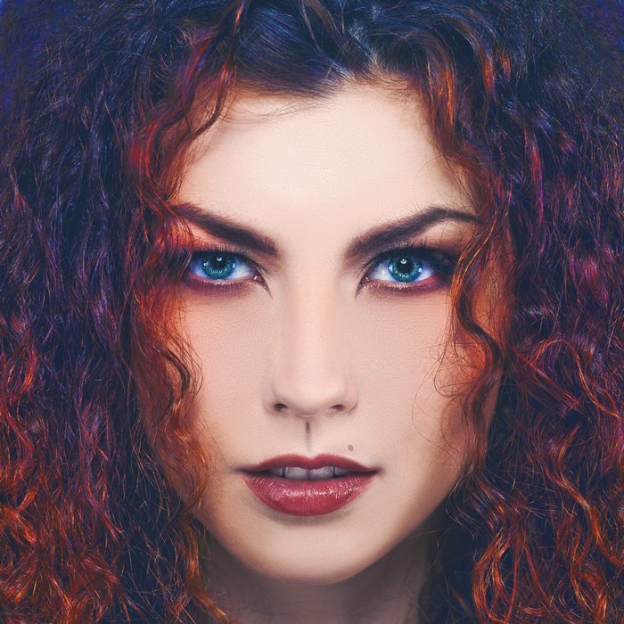 Close up portrait of a woman with curly red and black hair and blue eyes