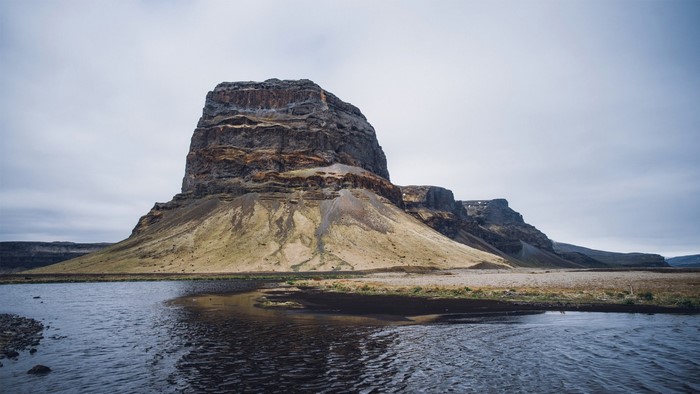 Flat-topped mountain formation by a river under a cloudy sky