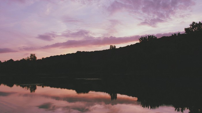 Sunset over a silhouetted hill and lake reflection